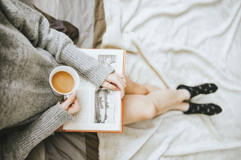 woman reading a book drinking coffee wearing a cozy sweater